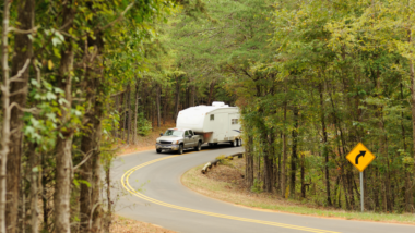 A truck tows a fifth wheel RV through a windy forest road. The truck has a B&W companion hitch so you know the fifth wheel RV is securely hitched.