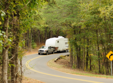 A truck tows a fifth wheel RV through a windy forest road. The truck has a B&W companion hitch so you know the fifth wheel RV is securely hitched.